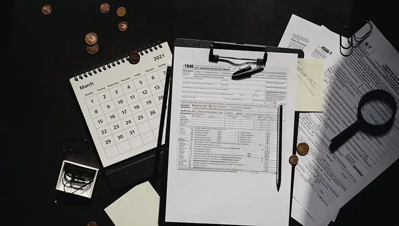 Starting a Business Overseas? A Quick Guide to Tax Considerations US Tax Forms rest among clipping board, a magnifying glass, a calendar, and coins.
