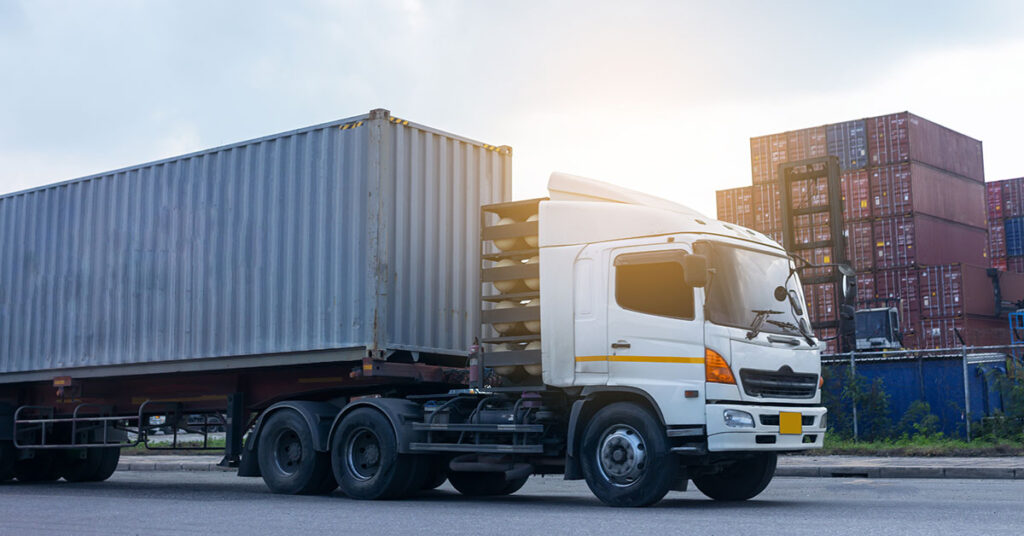 Commercial truck parked near shipping containers at a logistics hub, representing transportation business and zero down payment financing opportunities