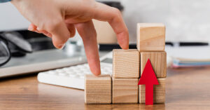 Hand walking up wooden blocks with an upward arrow symbolizing business growth, progress, and scaling success