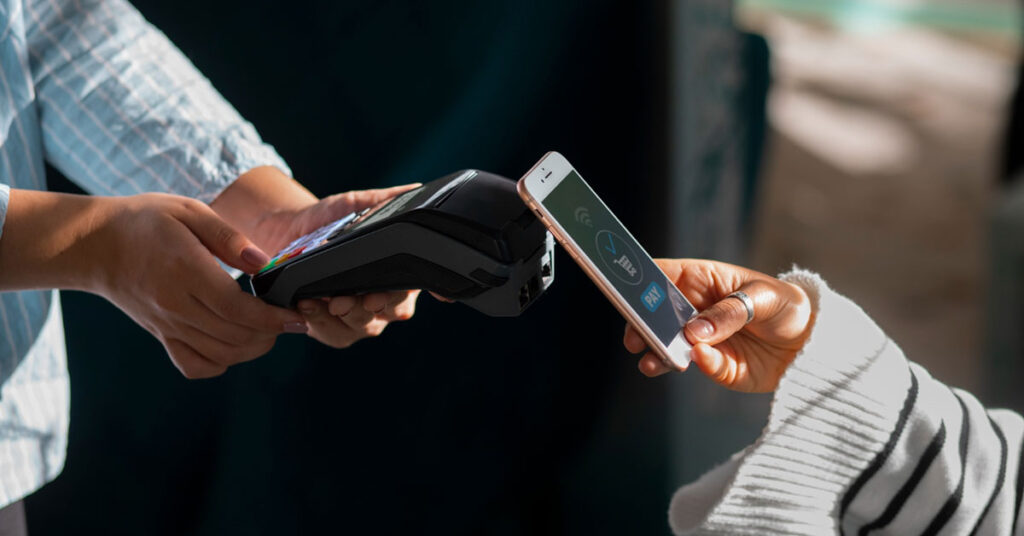 Close-up of a person making a contactless payment using a smartphone at a point-of-sale terminal, highlighting mobile payment security