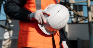 Close-up of a construction worker wearing safety gloves and holding a white hard hat, symbolizing safety and preparedness on a construction site
