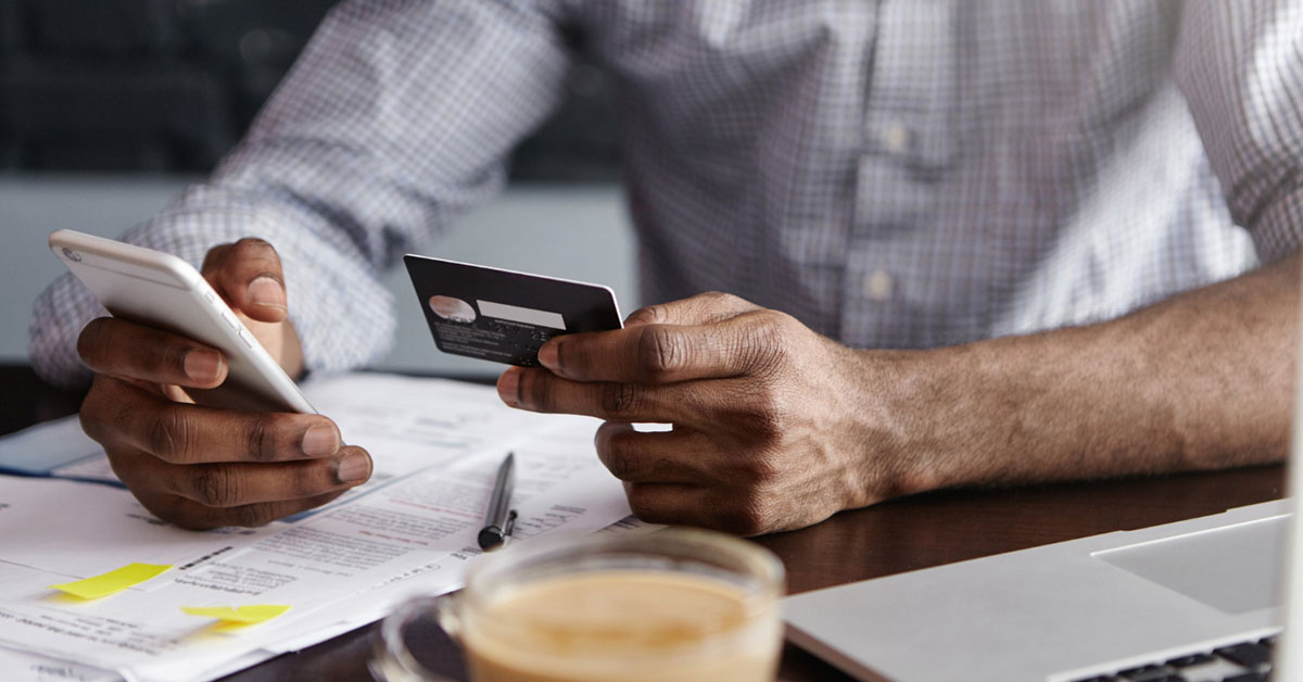 Close-up of person holding a credit card and smartphone while managing finances, symbolizing online credit repair and financial decision-making