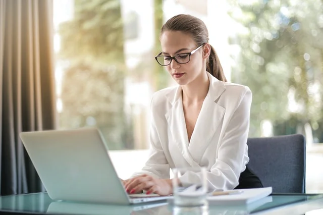Young business woman seated at her office desk, typing on a laptop computer.