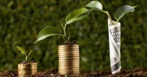 Three stages of plant growth emerging from stacks of coins and paper currency, symbolizing financial growth and investment impact