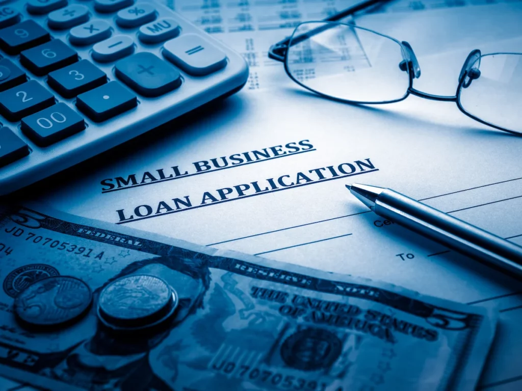 Money, calculator, a pen and glasses over a small business application form