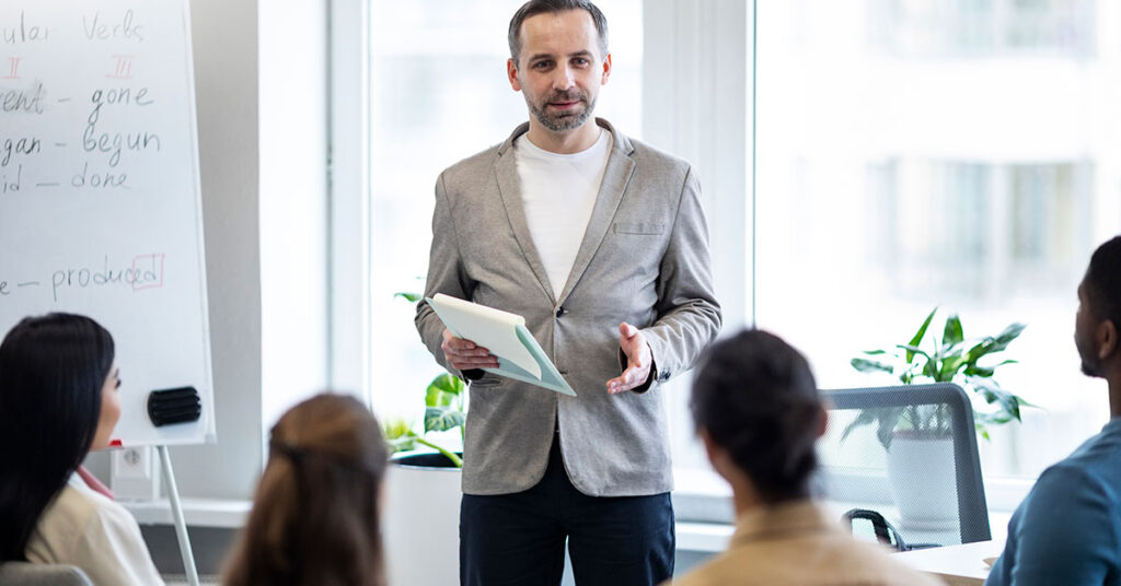 Professional business coach delivering a presentation to a group of attentive professionals in a modern office setting