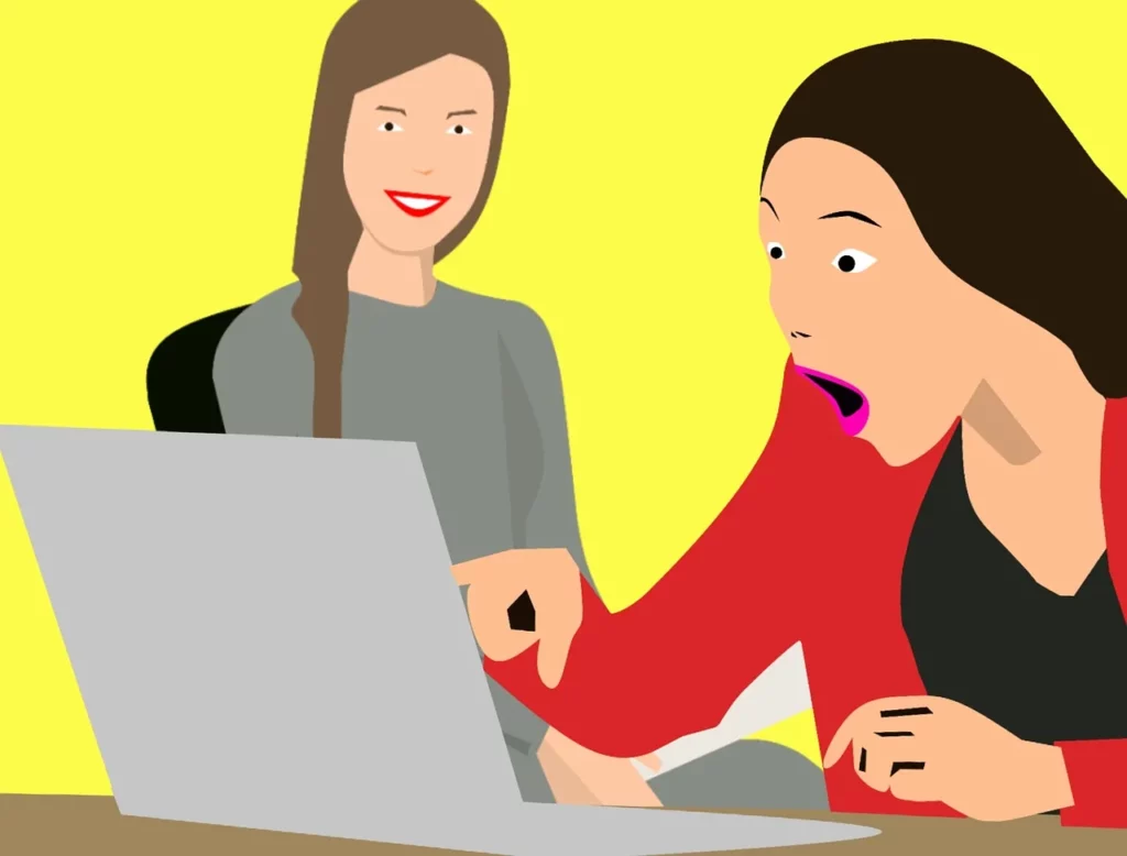 Two girls in front of a computer, one of them with a surprise expression