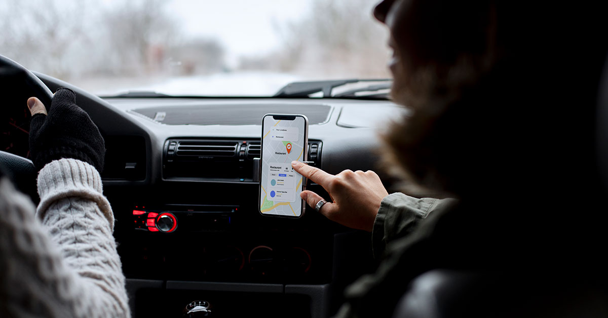 People traveling by car while using a GPS application on a smartphone mounted on the dashboard to search for directions or a restaurant location.