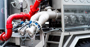 Close-up of industrial construction pump system with red and silver pipes and valve connections—illustrating key components to consider when selecting a pump for a construction job.