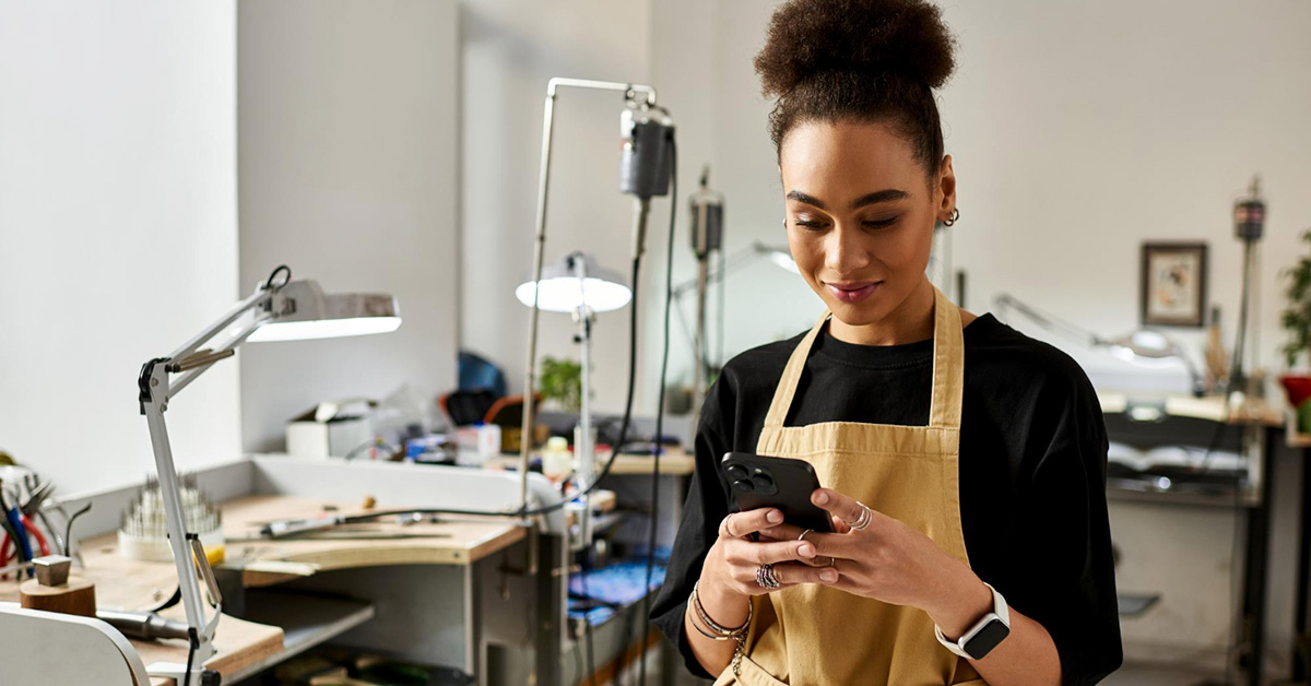 Small business owner in a workshop wearing an apron and using a smartphone—representing asset management and protection strategies for entrepreneurs.
