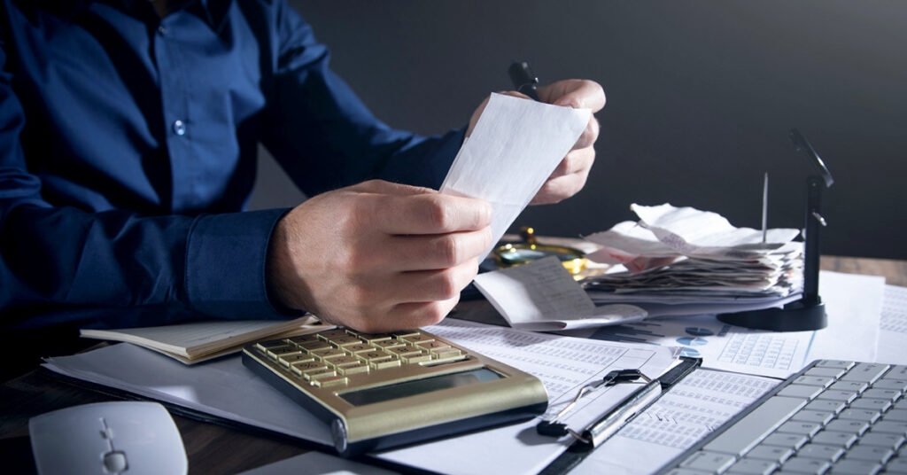 Close-up of a person reviewing financial receipts and using a calculator at a cluttered desk—illustrating the process of managing real estate transactions and understanding 1031 exchanges.