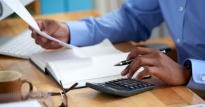 Close-up of a person reviewing financial documents with a calculator and notebook—depicting small business accounting and the role of a CPA.