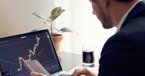 Man analyzing stock charts on a laptop and smartphone at a desk—illustrating the highs and lows of investing and the inevitability of failure in trading.
