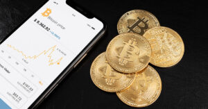Smartphone displaying Bitcoin price chart alongside golden Bitcoin coins on black background, representing cryptocurrency adoption in business payments.