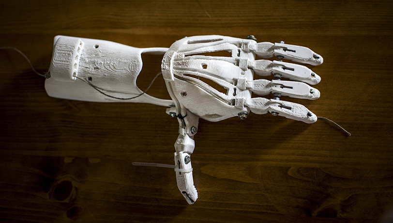 A 3D printed model of a prosthetic hand rests on a table, depicting the now common practice of 3D printing as a manufacturing process.