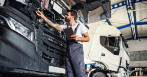Mechanic inspecting the engine of a commercial truck in a repair shop, representing business challenges and financial impact of commercial vehicle maintenance.