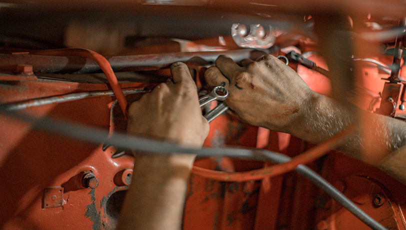 A man does maintenance work under the hood of an old commercial vehicle.