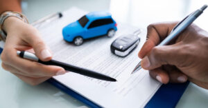 Close-up of hands signing a car insurance agreement with a toy car and car key on the contract, representing vehicle insurance considerations for small businesses.
