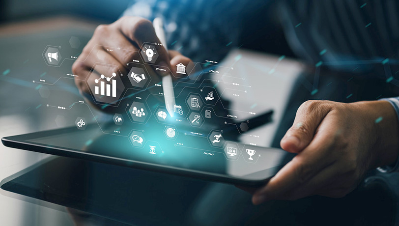 Image of a man taping the display of a tablet as it projects a hologram of several types of icons representing Marketing Automation.