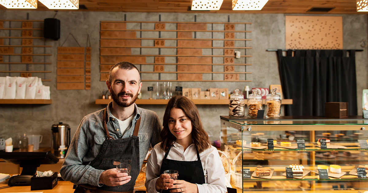 Smiling franchise business owners standing behind the counter of a modern café or bakery, representing the success and opportunities of franchise ownership and financing.