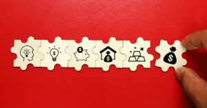 Row of wooden puzzle pieces with financial icons including idea, savings, investment, and money symbols—illustrating the multiple benefits of equipment leasing loans.