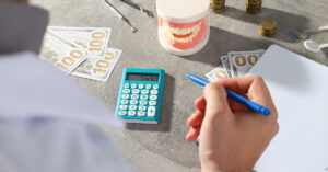 Close-up of dentist calculating financial costs with dental tools, money, and a dental model on the table, representing the financial planning involved in dental practice management.