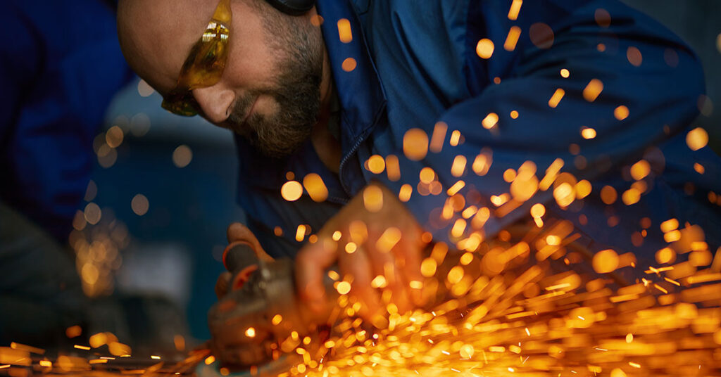 Close-up of a metal fabricator using an electric grinder, with bright sparks flying, symbolizing the skills, precision, and hard work required for success in fabrication.