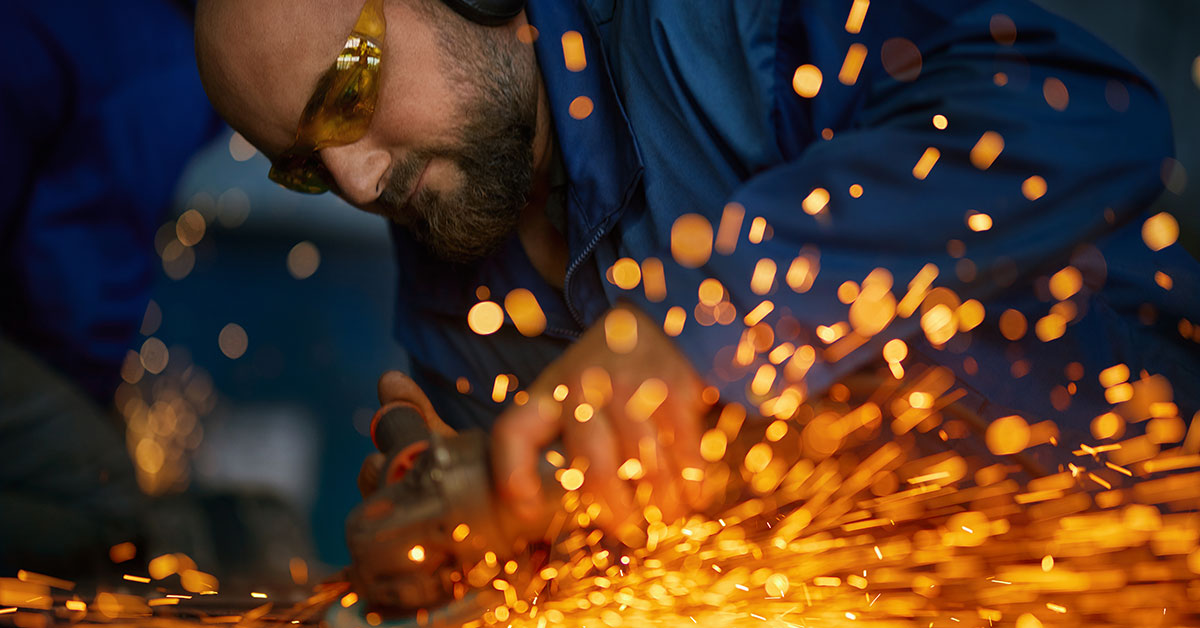 Close-up of a metal fabricator using an electric grinder, with bright sparks flying, symbolizing the skills, precision, and hard work required for success in fabrication.