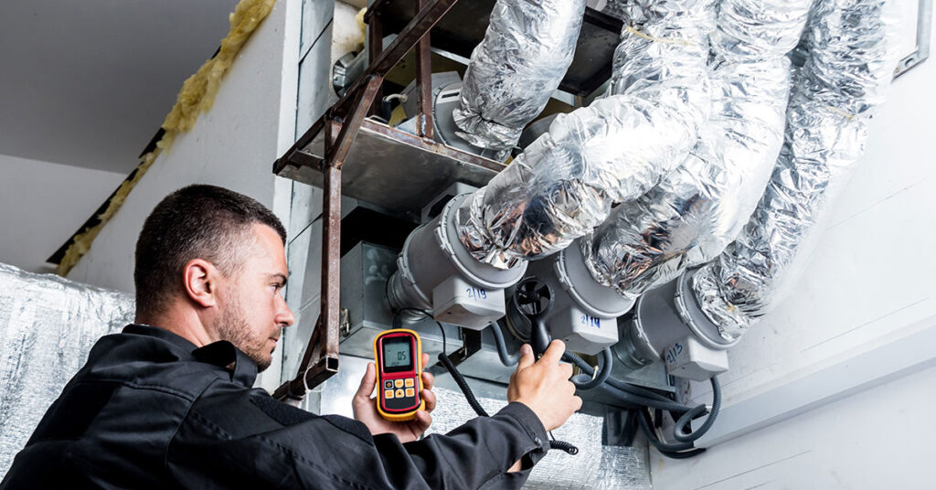 HVAC technician using an anemometer to measure airflow in a ventilation system, representing the need for working capital and equipment financing in the HVAC industry.