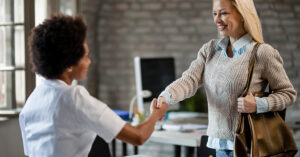 Two professional women shaking hands in an office, symbolizing a successful business agreement or the purchase of an existing business.