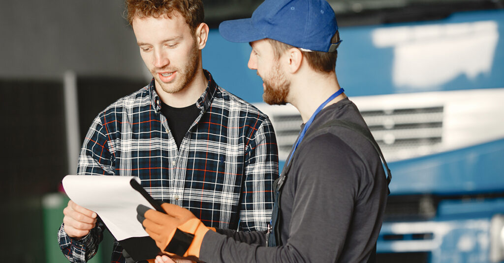 Two workers discussing documents near a truck, representing decision-making in equipment financing and leasing for businesses.
