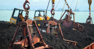Heavy construction equipment, including bulldozers and industrial cranes, handling coal or raw materials near a waterfront site—illustrating business assets that can be financed through equipment loans.