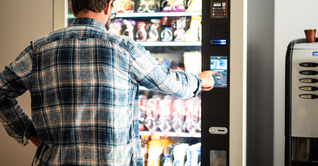 Man using a vending machine to select snacks or beverages, representing the vending industry and the financial opportunities for investing in vending and arcade machines.